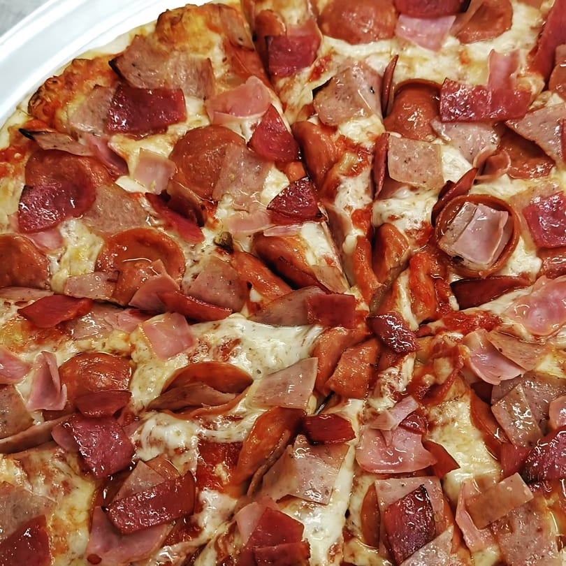 Close-up of a Jake's Pizza Rostraver pizza, loaded with pepperoni, ham, and sausage.