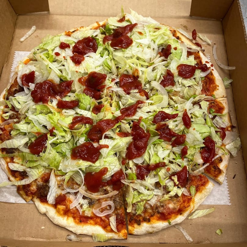 Jake's Pizza Rostraver taco pizza, topped with shredded lettuce, onions, and red sauce, in a box.