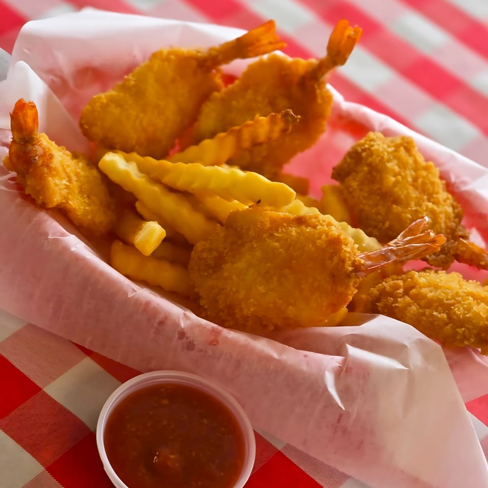 A basket of golden-brown fried shrimp and crinkle-cut fries with a side of dipping sauce.