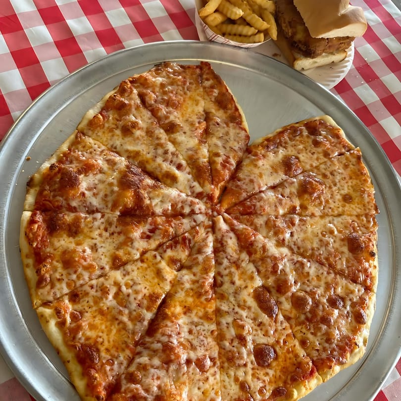 A large cheese pizza, cut into many slices, on a metal tray with fries and a sandwich.