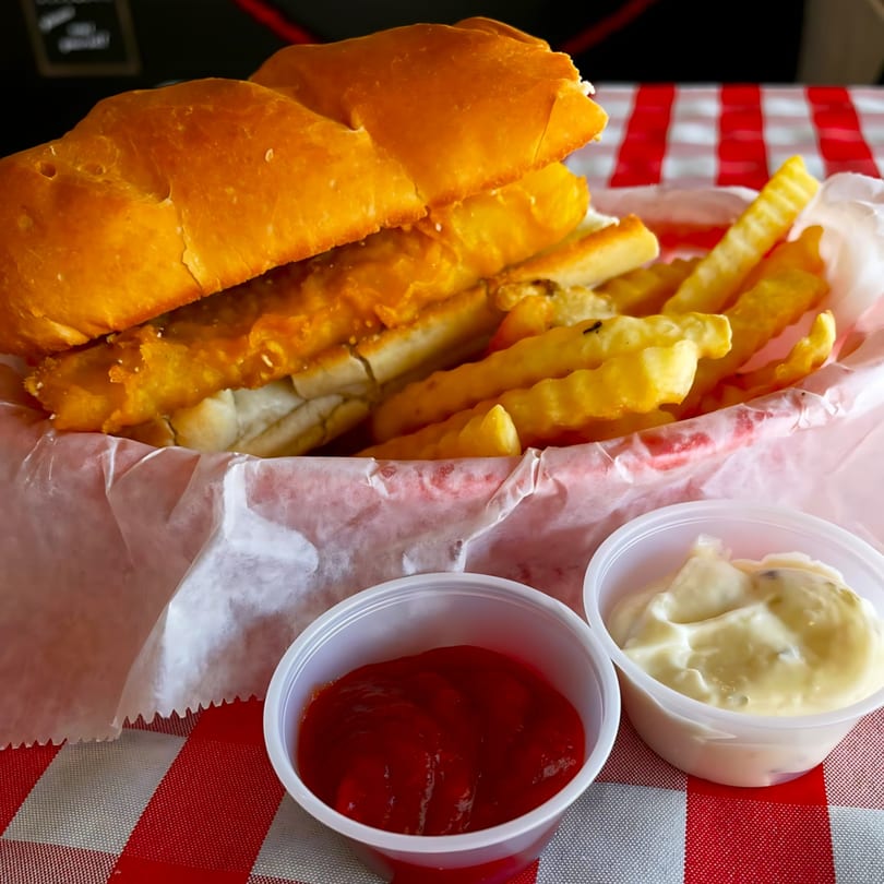 A fried fish sandwich and crinkle-cut fries in a basket with ketchup and tartar sauce.